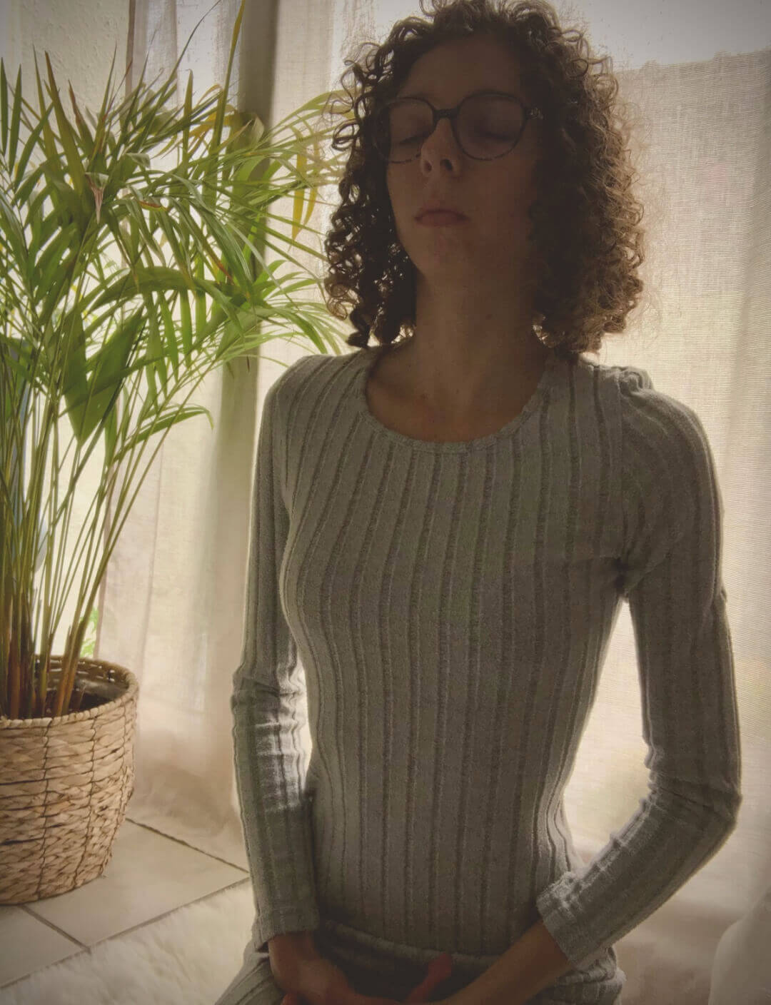 Femme en posture de relaxation, assise sur un tapis au sol, yeux fermés, dans une ambiance apaisante. Atelier bien-être et respiration pour futures mamans, jeunes mamans et femmes dans le Nord (Arras, Douai, Valenciennes, Orchies, Cambrai, Somain, Lens, Hénin-Beaumont...)
